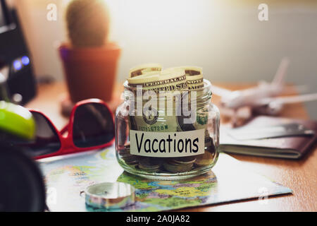 Vacation budget concept. Money for vacations savings in a glass jar with compass, passport, sunglasses, credit card and aircraft toy on world map Stock Photo