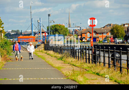 Couple with dogs walking along Riverside walk on Preston Docks on a warm sunny day Stock Photo