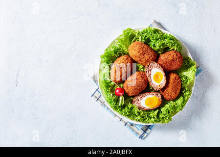 Traditional scotch eggs served with lettuce and radish on a white plate on a concrete table with napkin, view from above, flatlay, free space Stock Photo