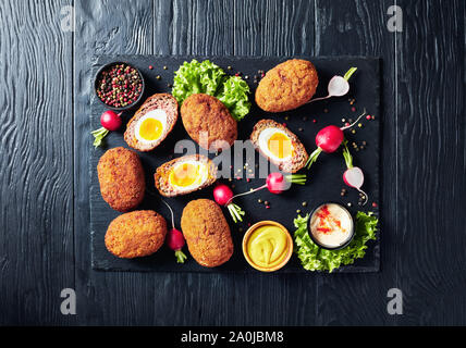 meatballs stuffed with soft boiled eggs, scotch eggs served with radish, mayonnaise and mustard on a black stone plate, view from above Stock Photo
