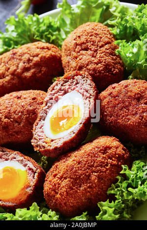 close-up of scotch eggs, boiled eggs wrapped in minced meat and deep fried, served with lettuce leaves on a plate, macro Stock Photo