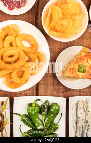 Spanish tapas, a variety of snacks. Squid rings, tortilla, sardines, padron peppers, top shot on a dark rustic wooden background Stock Photo