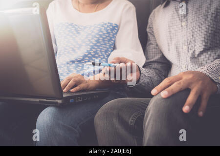Man and woman workmate in casual dress discussing together while using laptop and sitting on sofa in office. Stock Photo