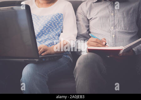 Man and woman workmate working together on laptop and notepad are sitting on sofa in office. Stock Photo