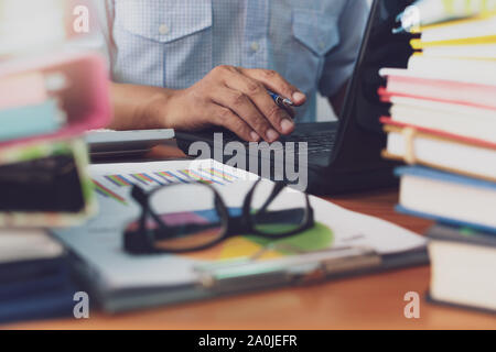 Man is using laptop and working with stack of documents on office desk, Businessman is analyzing marketing with statistics chart, Business and Office Stock Photo