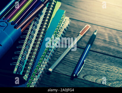 Heap of notebook with pens on wooden table under light in vintage style Stock Photo