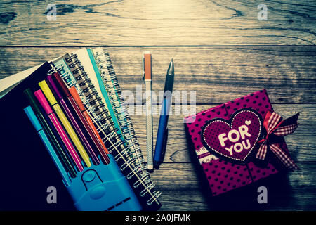 Gift box, notebooks and pens on wooden plank under light in vintage style Stock Photo
