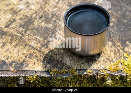 Cup of coffee or tea on a moss covered tree stump in sunlight in the woods (angled side view, horizontal format) Stock Photo