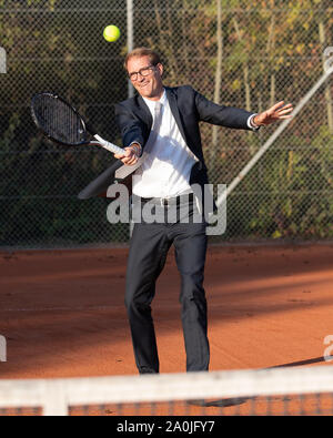 Smiling businessman in dark suit playing tennis Stock Photo