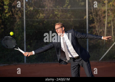 Smiling businessman in dark suit playing tennis Stock Photo