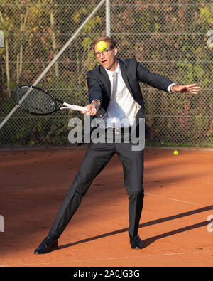 Smiling businessman in dark suit playing tennis Stock Photo