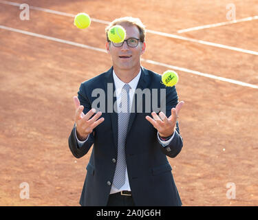 Elevated view of smiling businessman in dark suit juggling with tennis balls on tennis court Stock Photo