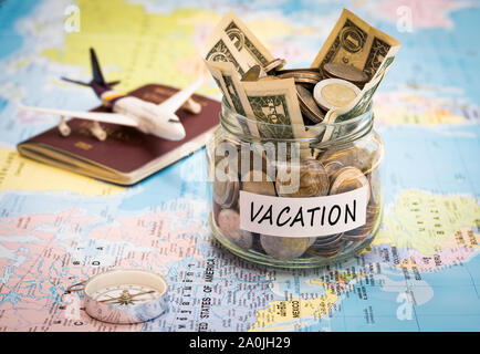 Vacation budget concept. Vacation money savings in a glass jar with compass, passport and aircraft toy on world map Stock Photo