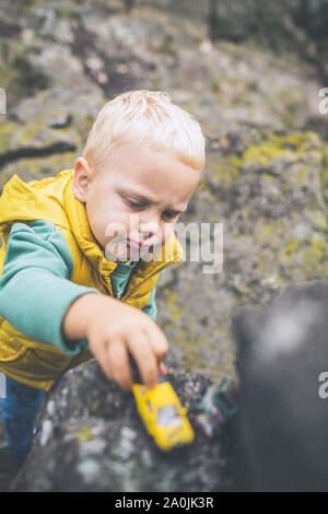 Toddler boy playing with toys on a rock. Little child walking on rocky mountains. Stock Photo