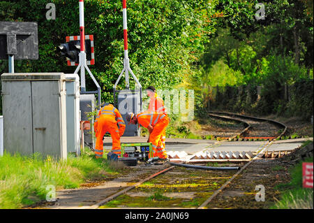 Three engineers in orange overalls working on traffic crossing area of Preston steam railway running along Preston docks and marina Stock Photo