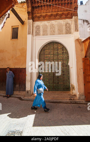 woman in traditional clothing walking past ornate mosque door in the medina of fes morocco Stock Photo