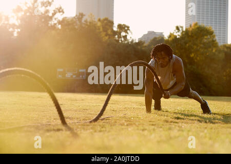 African-American man working out with battle ropes in field Stock Photo