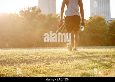 African-American man walking across field in urban park Stock Photo
