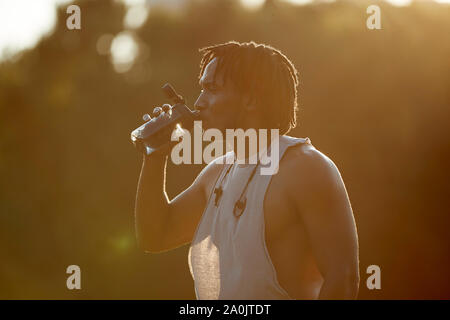 Thirsty African-American man drinking from water bottle in sunlight Stock Photo