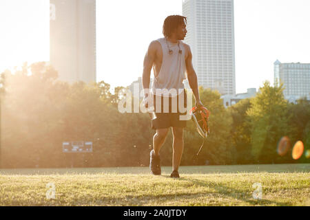 African-American man walking across field in urban park Stock Photo