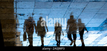 Blurry reflection shadow silhouette on wet city sidewalk of mysterious people walking away the night, low angle view Stock Photo