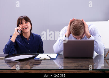 Businessman Irritated With Female Colleague Taking On Mobile Phone At Work In Office Stock Photo