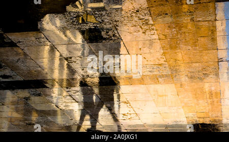 Blurry abstract shadow silhouette reflections of two people walking  on wet city street pavement Stock Photo