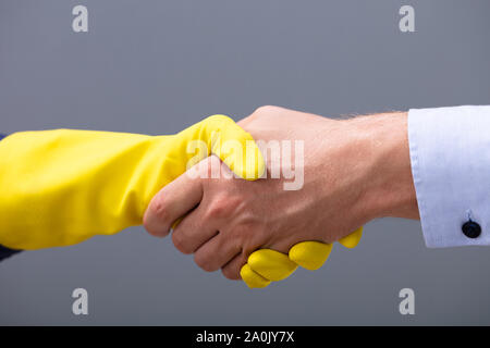 Close-up Of Businessman And Janitor Shaking Hands Together Against Gray Background Stock Photo