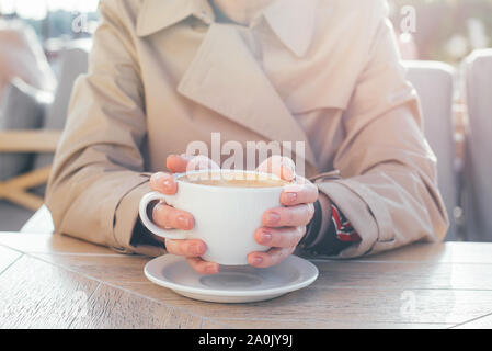 Big white coffee cup in woman's hands with pastel manicure while sitting in cafe. Stock Photo