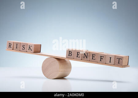 Close-up Of Risk And Benefit Wooden Blocks On Seesaw Against Reflective Desk Stock Photo