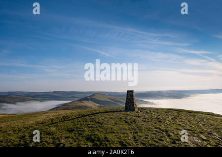 Trig point on top of Mam Tor, Peak District, UK. Early morning with mist in Edale and Hope Valley, and the Great Ridge rising above the mist Stock Photo