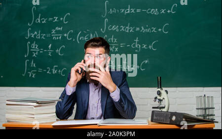 Calling parents. Call colleague ask advice. Pedagogue keep in touch with colleagues. School teacher call mobile phone while sit classroom chalkboard background. Teacher bearded man talk mobile phone. Stock Photo