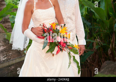 Partial view of a French couple wearing traditional white formal wedding attire holding native flowers during their wedding service outdoors in Domini Stock Photo