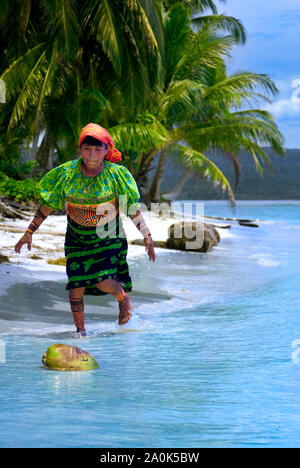 Kuna Indian woman wearing a traditional mola blouse, print skirt and red head scarf chases a coconut in the sea along the coast, Kuna (Guna)Yala/San B Stock Photo