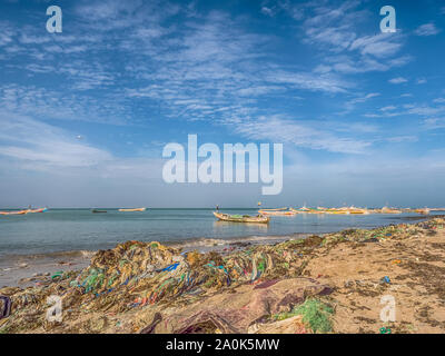Senegal, Africa - January 26, 2019: Plenty of plastic bags on shore of the ocean. Pollution concept. Colorful fisher boats in the background. Senegal. Stock Photo