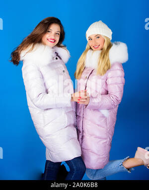 Women wear down jacket with furry hood. Girls smiling makeup faces wear  winter jackets blue background. Fashion friends. Winter season. Soft fur.  For those wishing stay modern. Winter clothes Stock Photo 