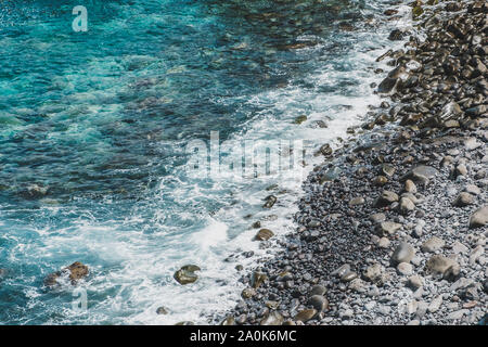 ocean waves on stone beach with black pebbles at rocky coast - Stock Photo