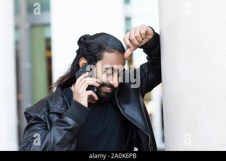 young man talking with smartphone holding arm on a wall Stock Photo
