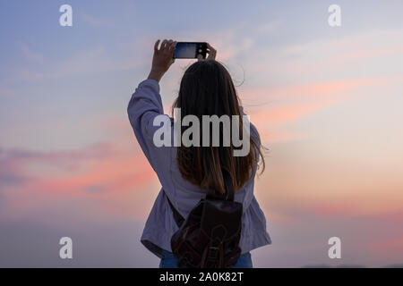 Young woman is taking a picture of the sky with her smartphone Stock Photo