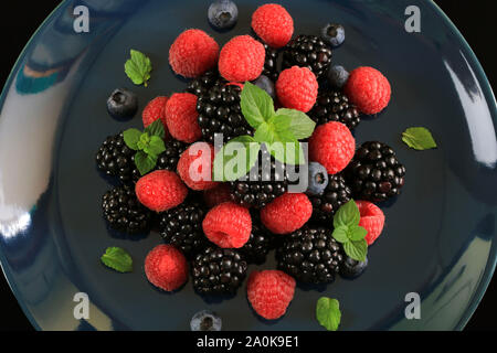 Plate with fresh raspberries, blackberries and blueberries with mint leaves isolated on dark background. Top view Stock Photo