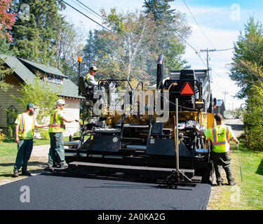 A dump truck and a paving machine laying new asphalt on a village street in Speculator, NY USA in early autumn Stock Photo