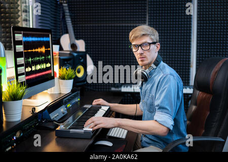 Young man with headphones looking at you while sitting in recording studio Stock Photo