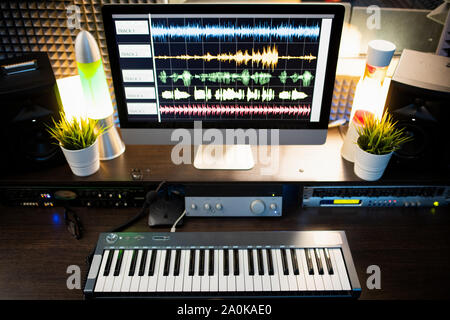 Piano keyboard and computer screen with waveform sound visualization on desk Stock Photo