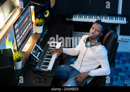 Young Afroamerican man in casualwear looking at you while sitting in studio Stock Photo