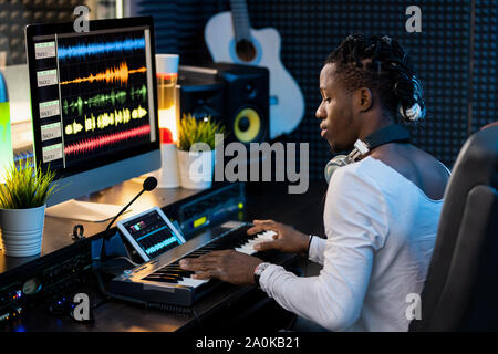 Serious young African man pressing keys of piano keyboard in sound record studio Stock Photo