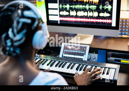 African or mixed-race young man touching keys of piano keyboard by computer Stock Photo