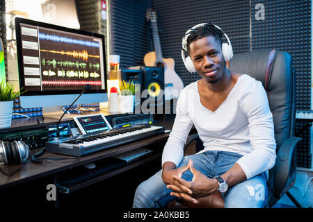 Happy young successful musician or producer in headphones sitting by workplace Stock Photo