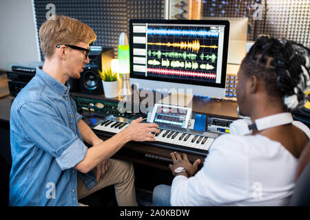 Two young multicultural musicians discussing new way of mising sounds in studio Stock Photo