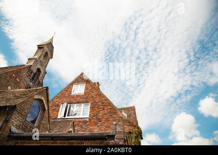 Rooftop of an old historic church and tiled facade house, blue cloudy sky in England, UK Stock Photo