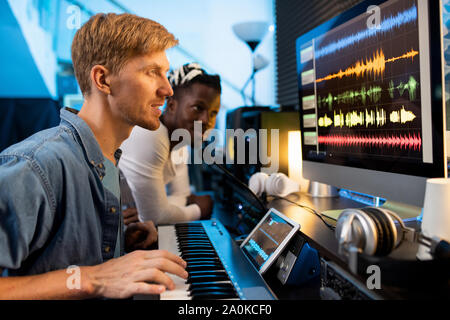 Young man with pianoboard looking at computer screen during work in studio Stock Photo